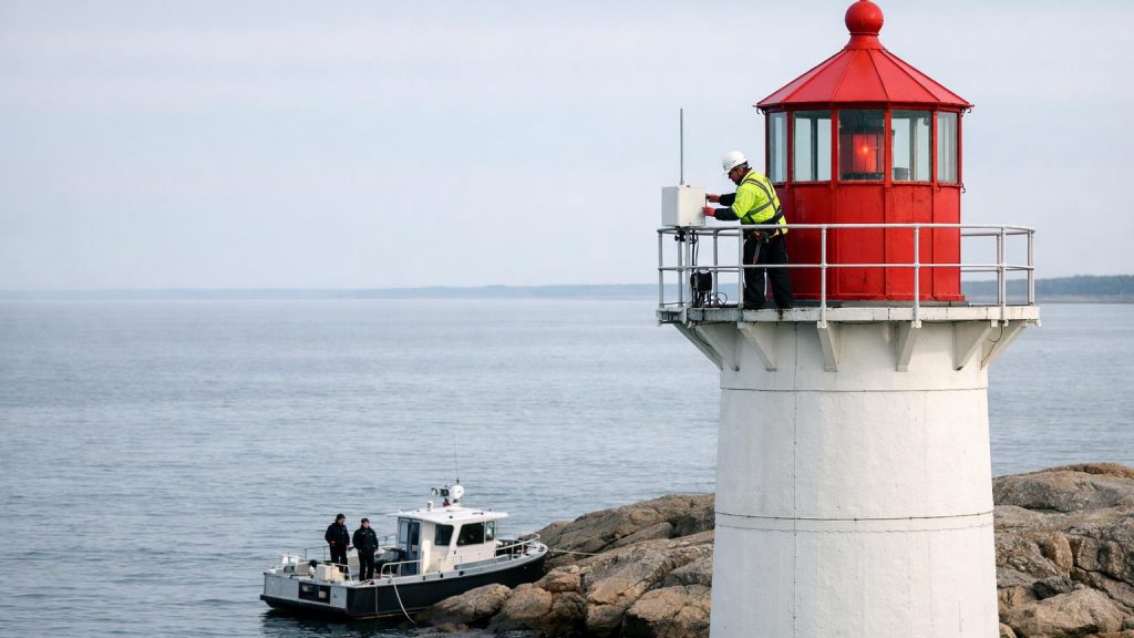 Vit fyr vid Östersjön med tekniker i säkerhetssele som installerar radarbox